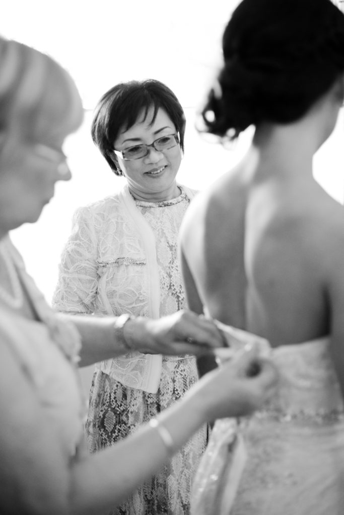 mother of the bride watching as bride gets dress on